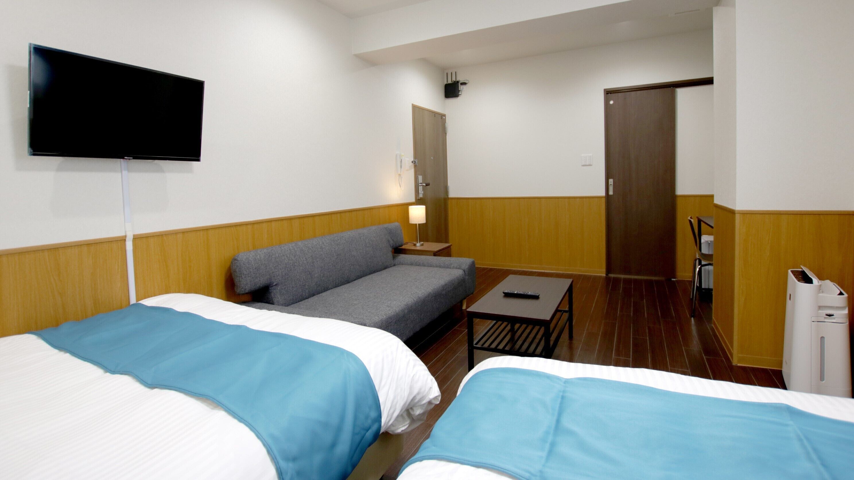 Habitació d'hotel amb dos llits, un sofà, un televisor, un escriptori i una porta.