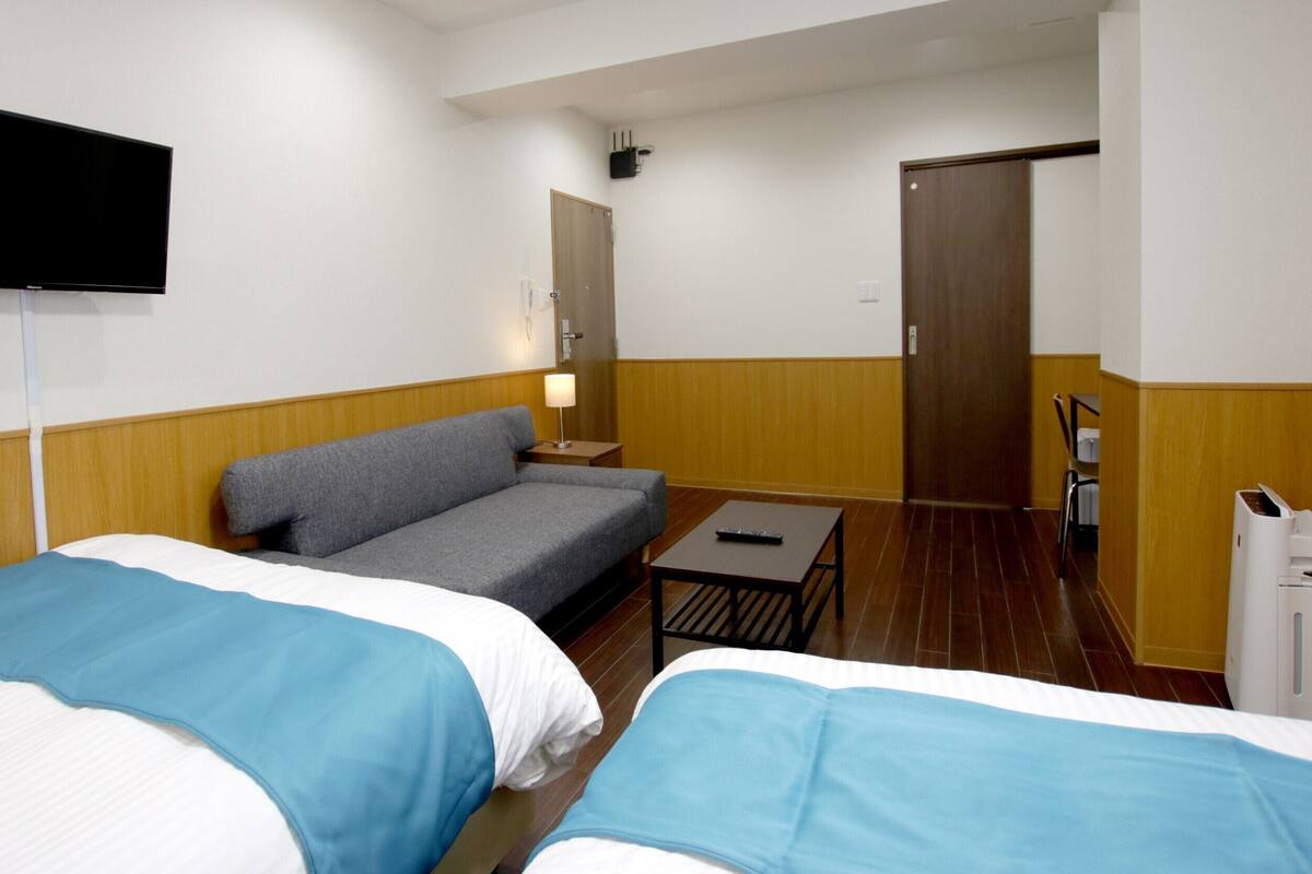 A hotel room with two beds, a sofa, a TV, a desk, and a door.