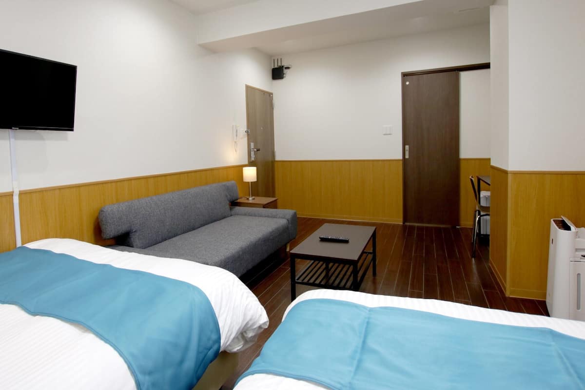 A hotel room with two beds, a sofa, a TV, a desk, and a door.
