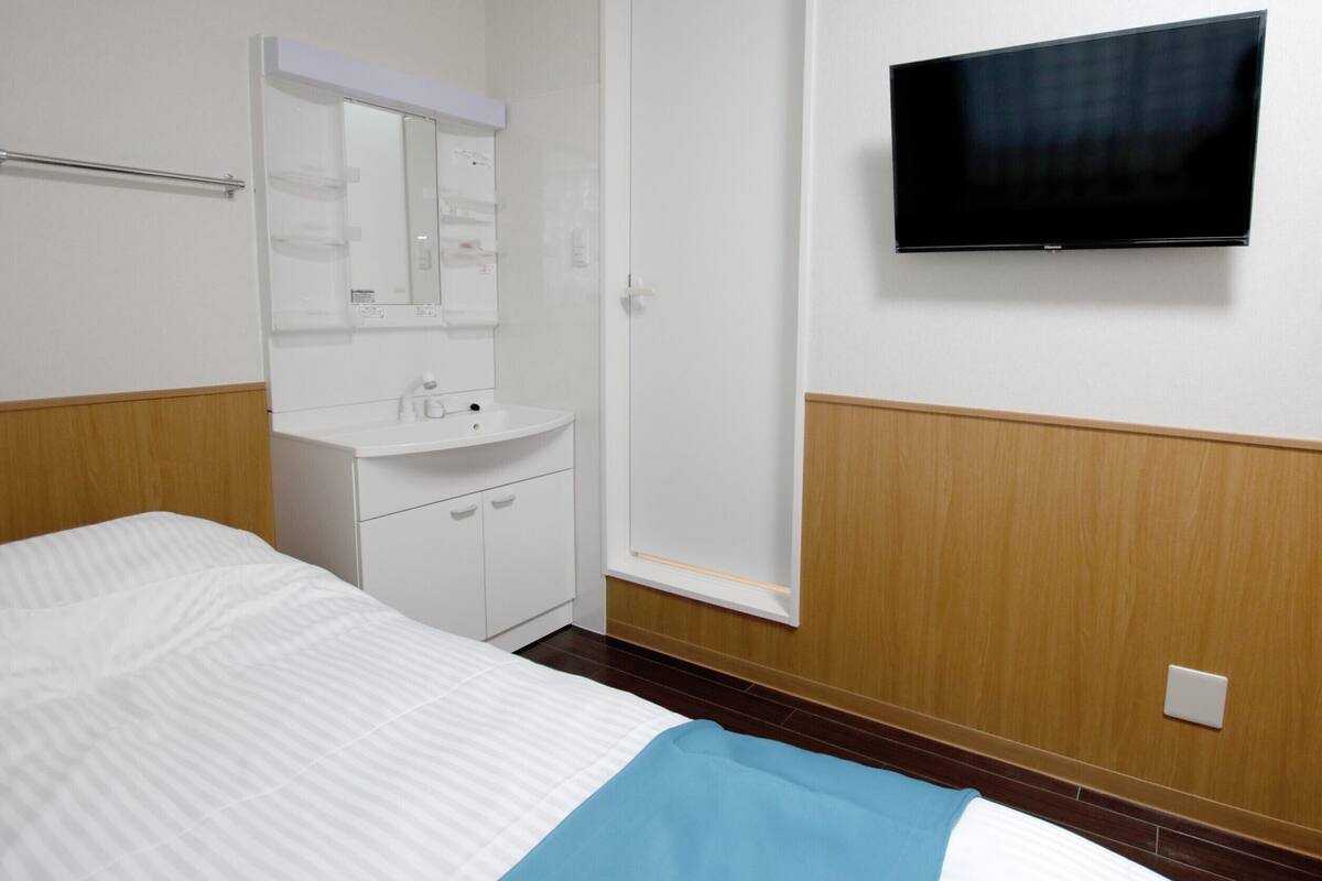 A hotel room with a bed, a bedside table, a mirror, a TV, and a telephone.
