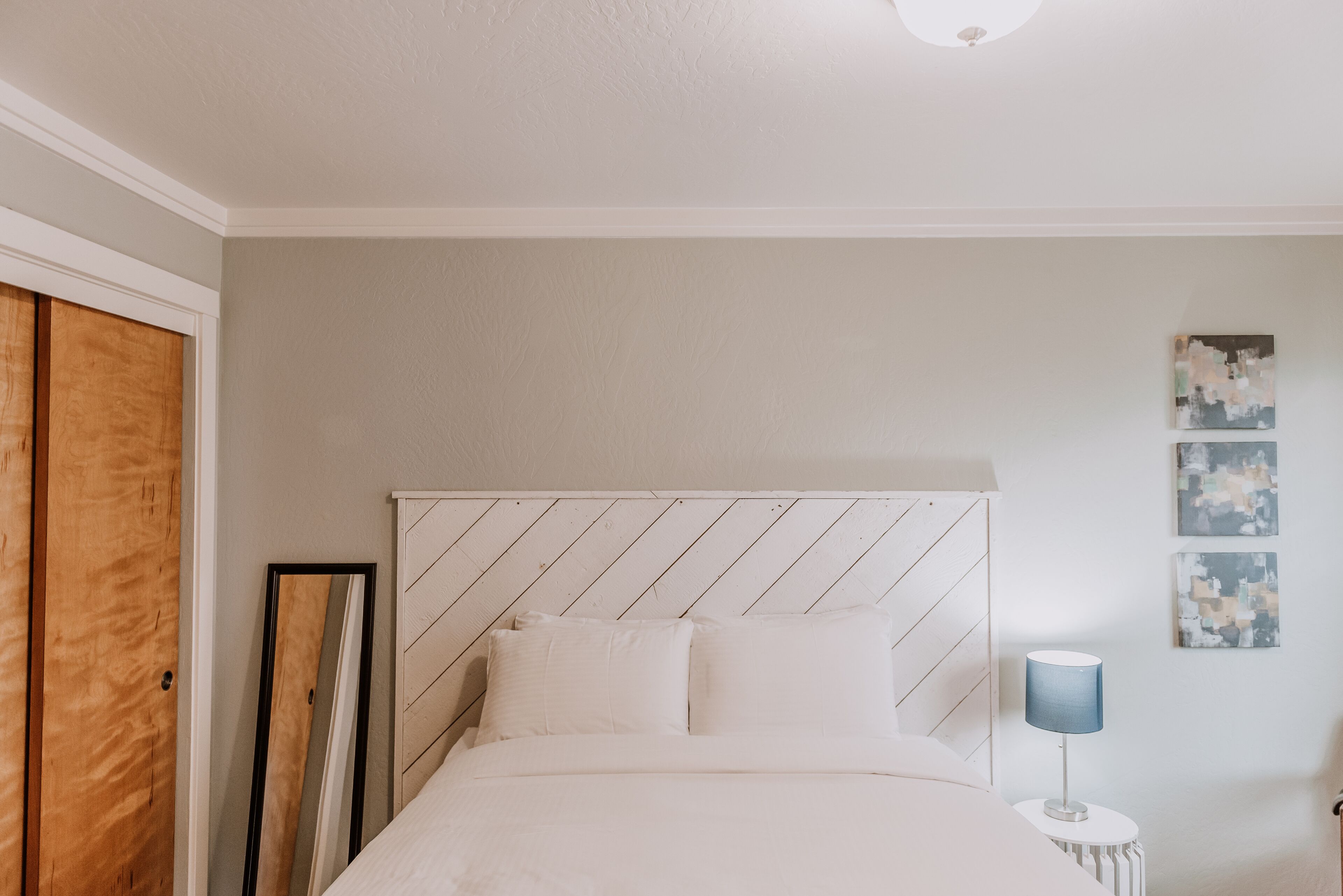 Un dormitorio con cama, armario de madera, espejo y una mesita con lámpara.