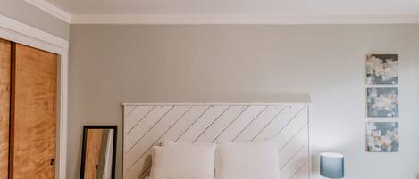 Un dormitorio con cama, armario de madera, espejo y una mesita con lámpara.
