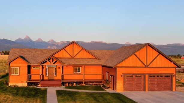 A large, two-story wooden house with a prominent front porch and garage, set against a mountainous backdrop. - Beautiful Family Getaway with Breathtaking Teton Views (Tetonia)