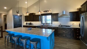 A modern kitchen with dark wood cabinets, a large island with bar stools, stainless steel appliances, and pendant lighting. - Beautiful Family Getaway with Breathtaking Teton Views (Tetonia)