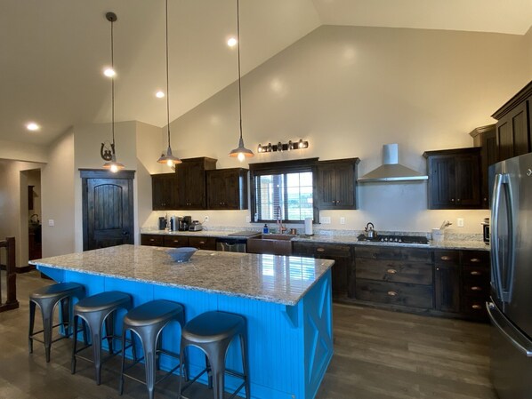 A modern kitchen with dark wood cabinets, a large island with bar stools, stainless steel appliances, and pendant lighting.