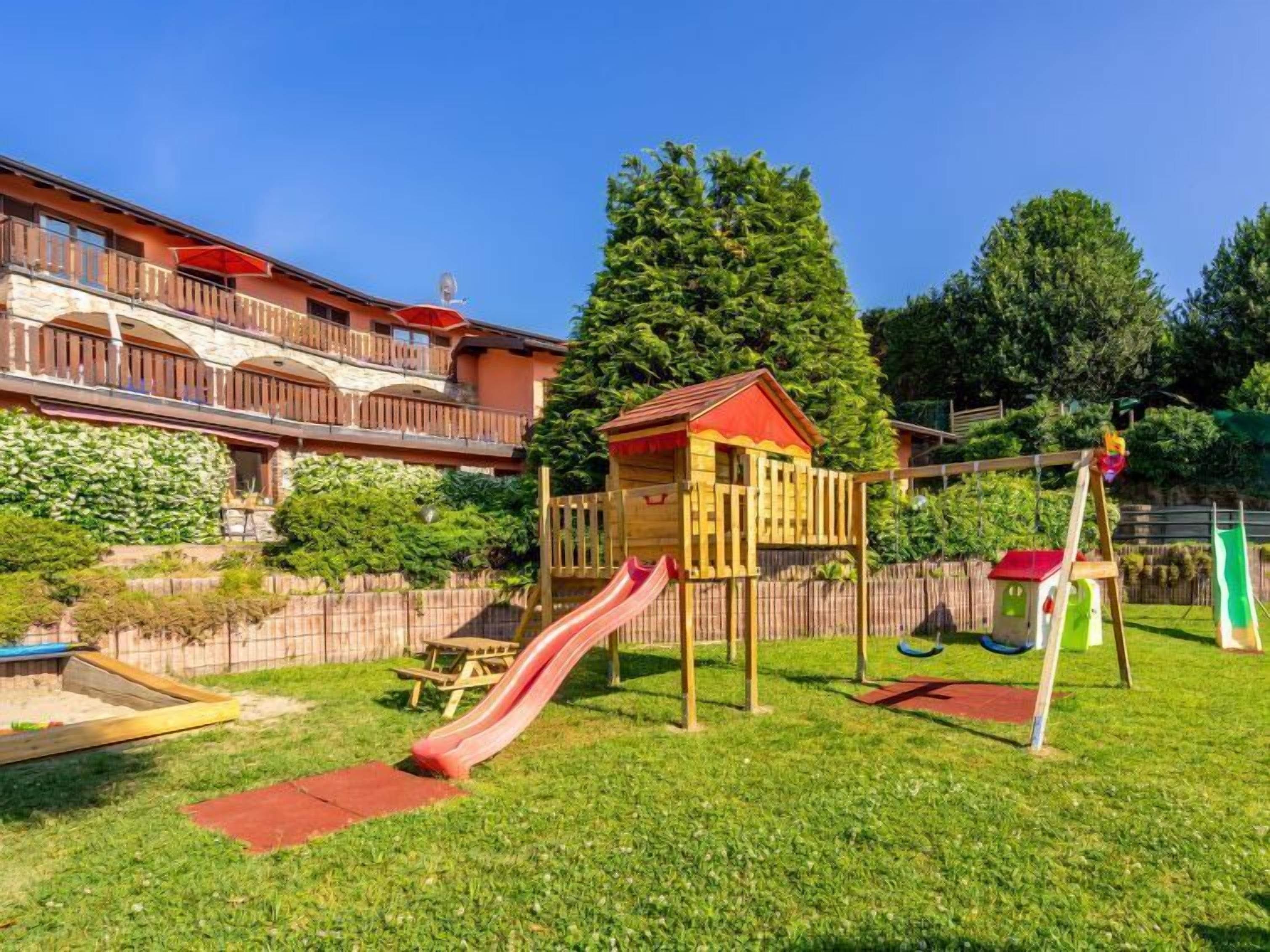 A playground with slides and swings, surrounded by a wooden fence and a building with balconies.