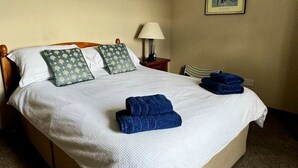 A neatly made bed with pillows and folded towels, a bedside lamp, and a framed picture on the wall.