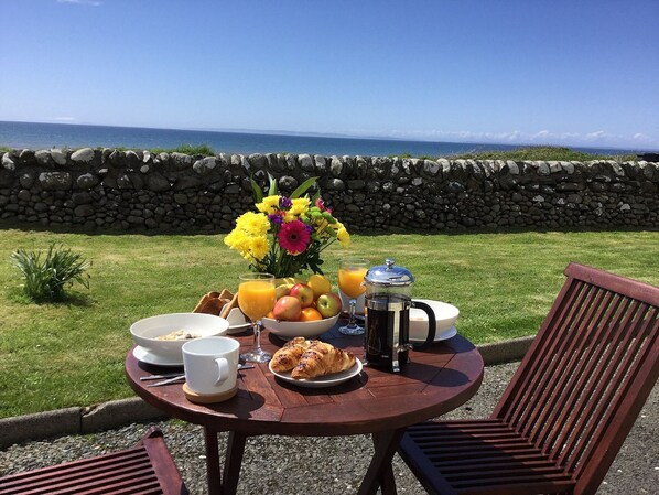 Desayuno preparado con pared de piedra, una mesa con alimentos para el desayuno y vista al océano.
