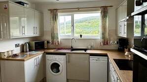 A compact kitchen with a washing machine, dishwasher, and a window with curtains.