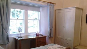 Une chambre à coucher avec un lit, un bureau doté d’un miroir, une armoire et une fenêtre avec des rideaux.