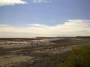 A coastal landscape with a flat terrain, a distant horizon, and a clear sky with scattered clouds.