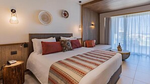 A hotel room with a large bed, bedside tables, a small round table, and a view of the outdoors through sheer curtains. - Minos All Suites (Rethymno)