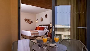 A hotel room with a bed, a round table with two chairs, and a balcony with a view. - Minos All Suites (Rethymno)