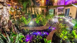 Ein Innenhofgarten mit Wasserspiel, hängenden Pflanzen und einem Balkon mit Geländer.