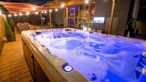Ein Whirlpool mit einer Holzterrasse und einem an der Wand befestigten Fernseher.
