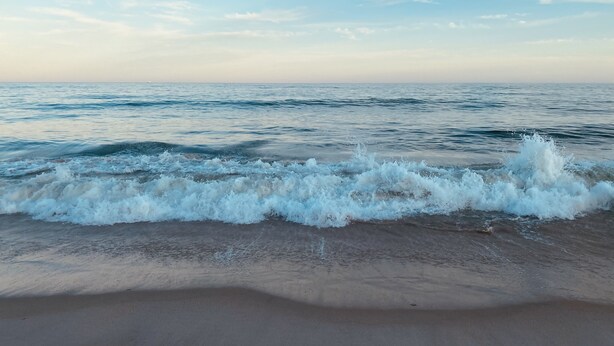 Une plage où les vagues se brisent sur le rivage, sous un ciel dégagé.