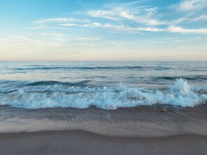 A beach with waves crashing onto the shore and a clear sky above.