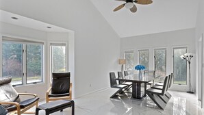 Une pièce spacieuse comprenant une table à manger, des chaises, un ventilateur de plafond et de grandes fenêtres.