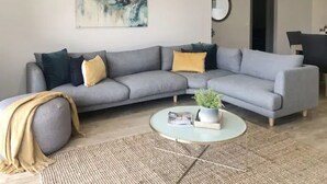 A modern living room with a grey sectional sofa, a round coffee table, and a large abstract painting on the wall. - New Torquay Beaches Deakin Uni Hospitals (Armstrong Creek)