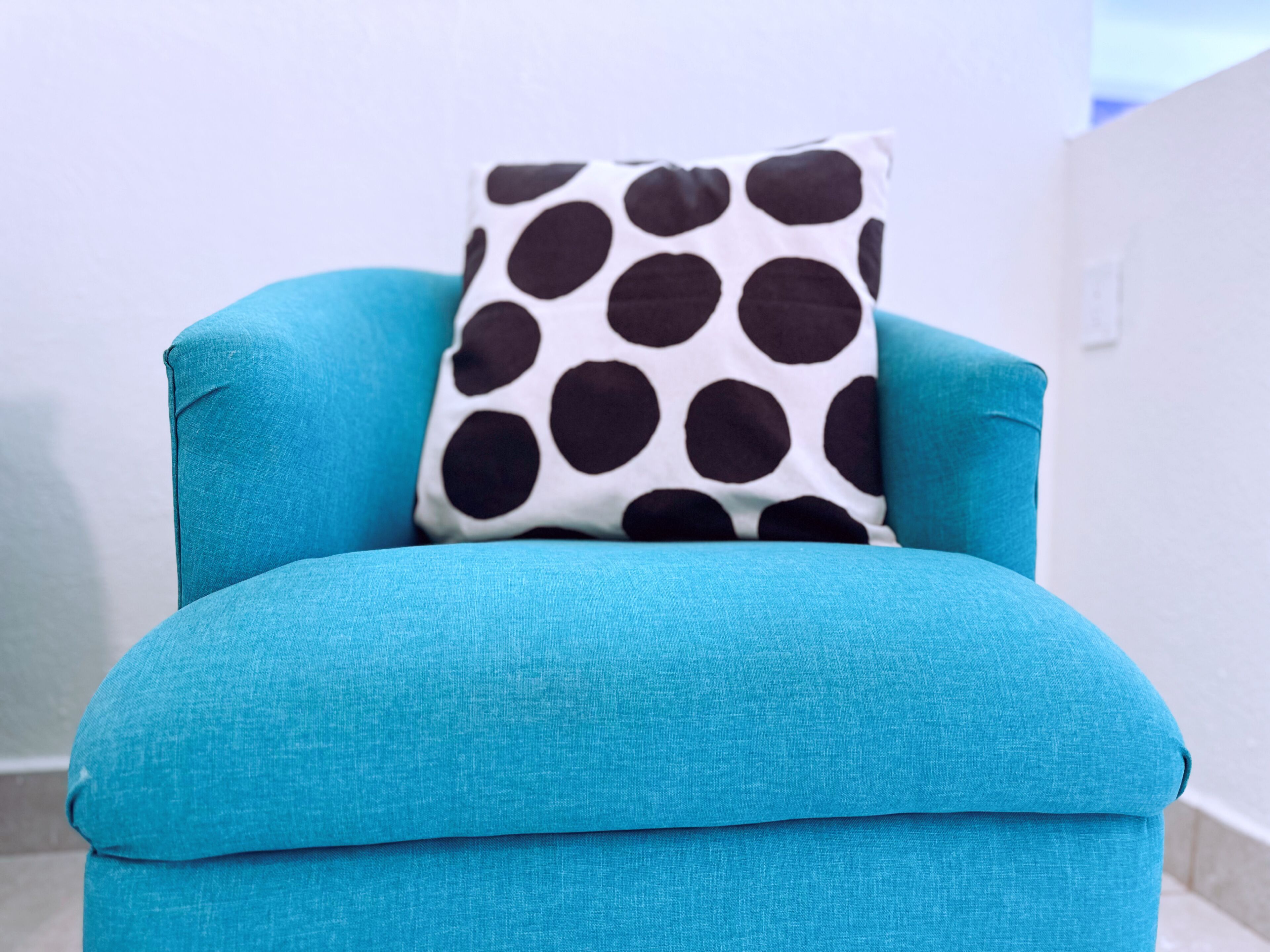 A teal armchair with a polka-dotted pillow.
