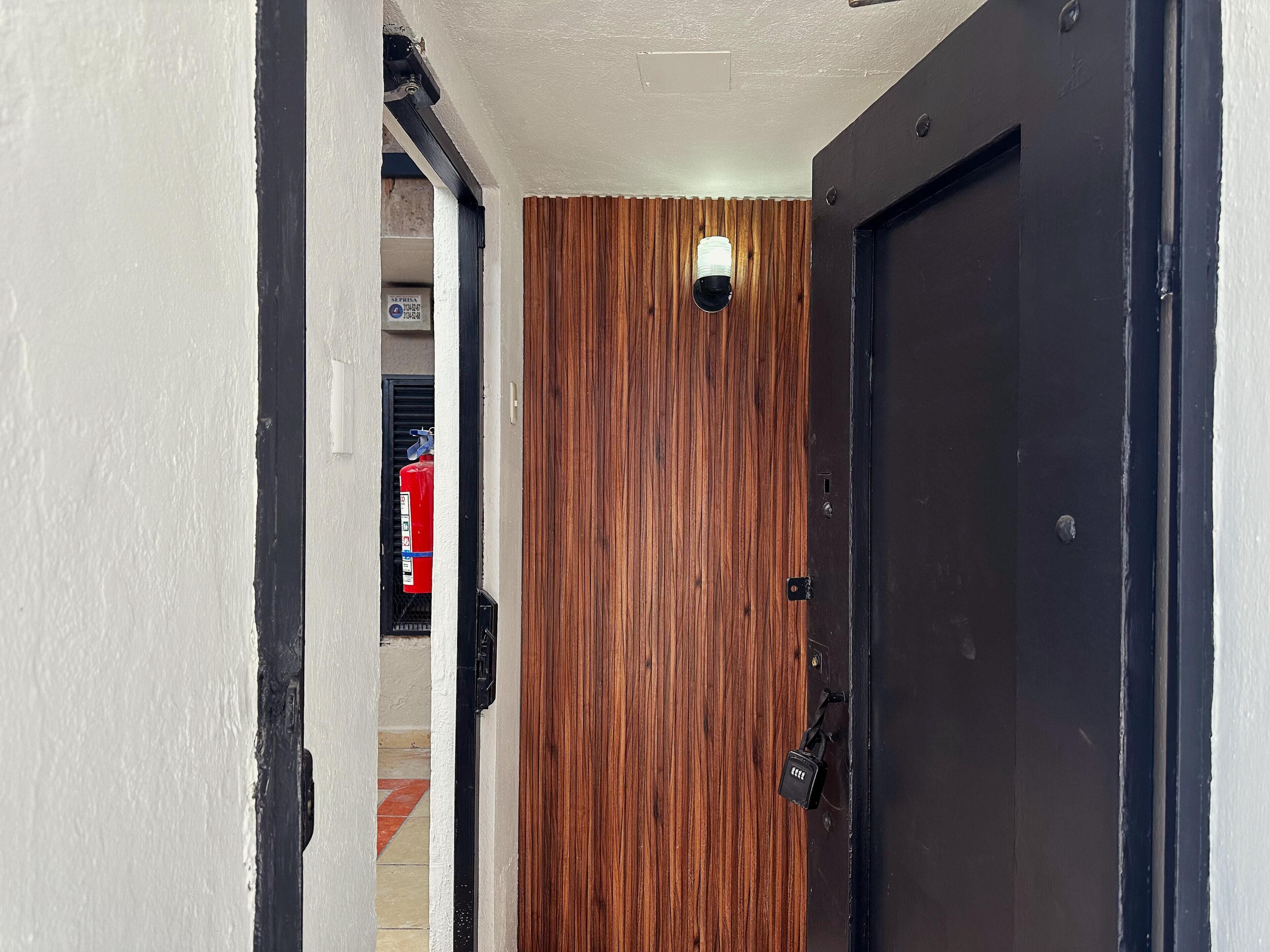 A hallway with a wooden wall, a black door, and a red fire extinguisher mounted on the wall.