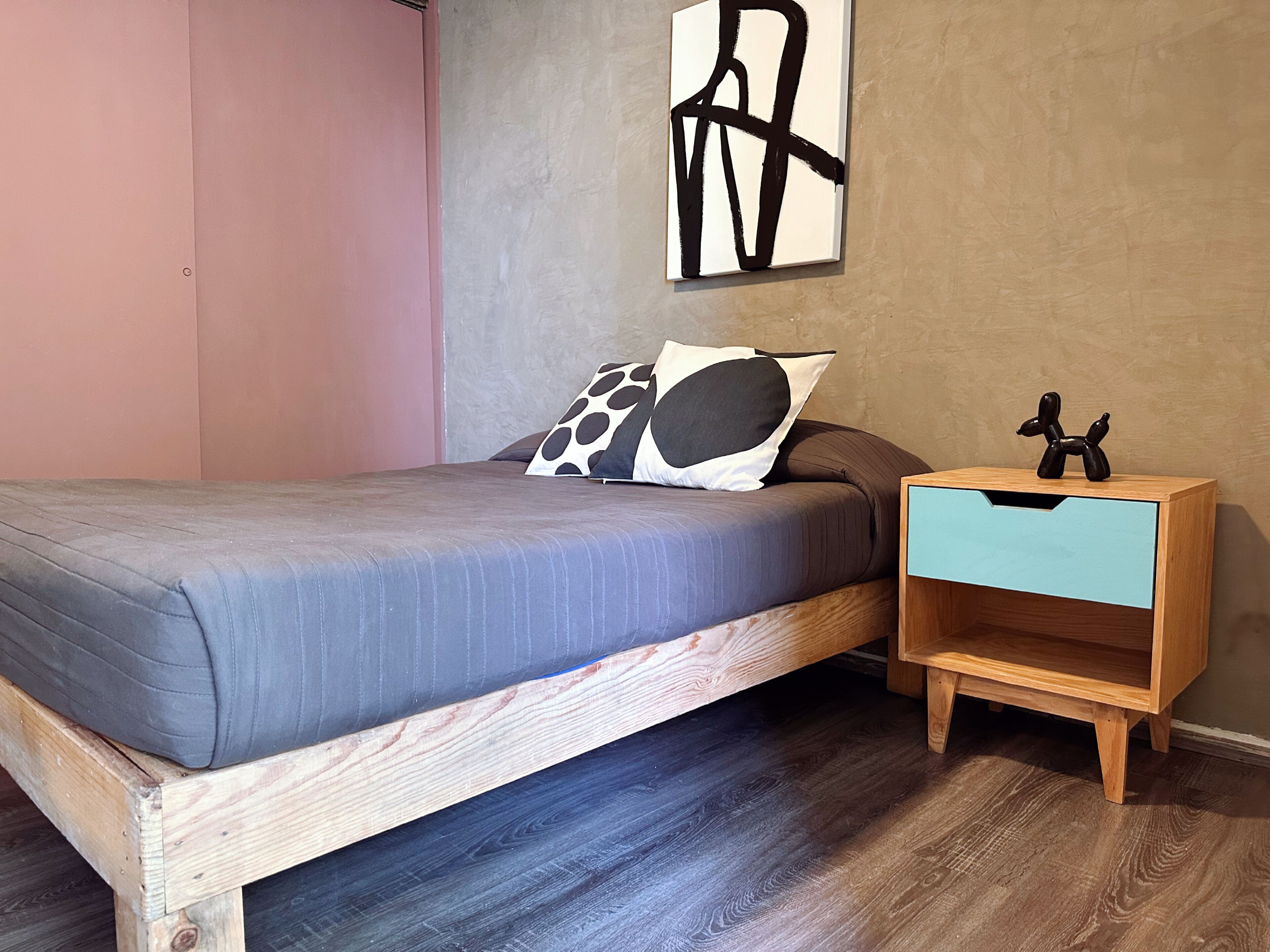 A bedroom with a bed, a nightstand, a wall art piece, and a wooden floor.