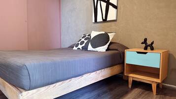 A bedroom with a bed, a nightstand, a wall art piece, and a wooden floor.