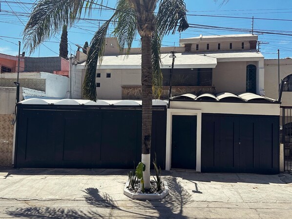 A residential area with a gated entrance, a palm tree, and a building with a flat roof and multiple windows. - Spacious 8-bedroom House in Central Guadalajara (Guadalajara)