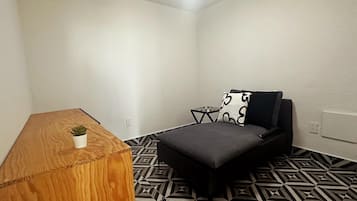 Una habitación pequeña y moderna con una mesita de madera, una planta pequeña en maceta, un sofá con estampado blanco y negro y un suelo con diseño geométrico.