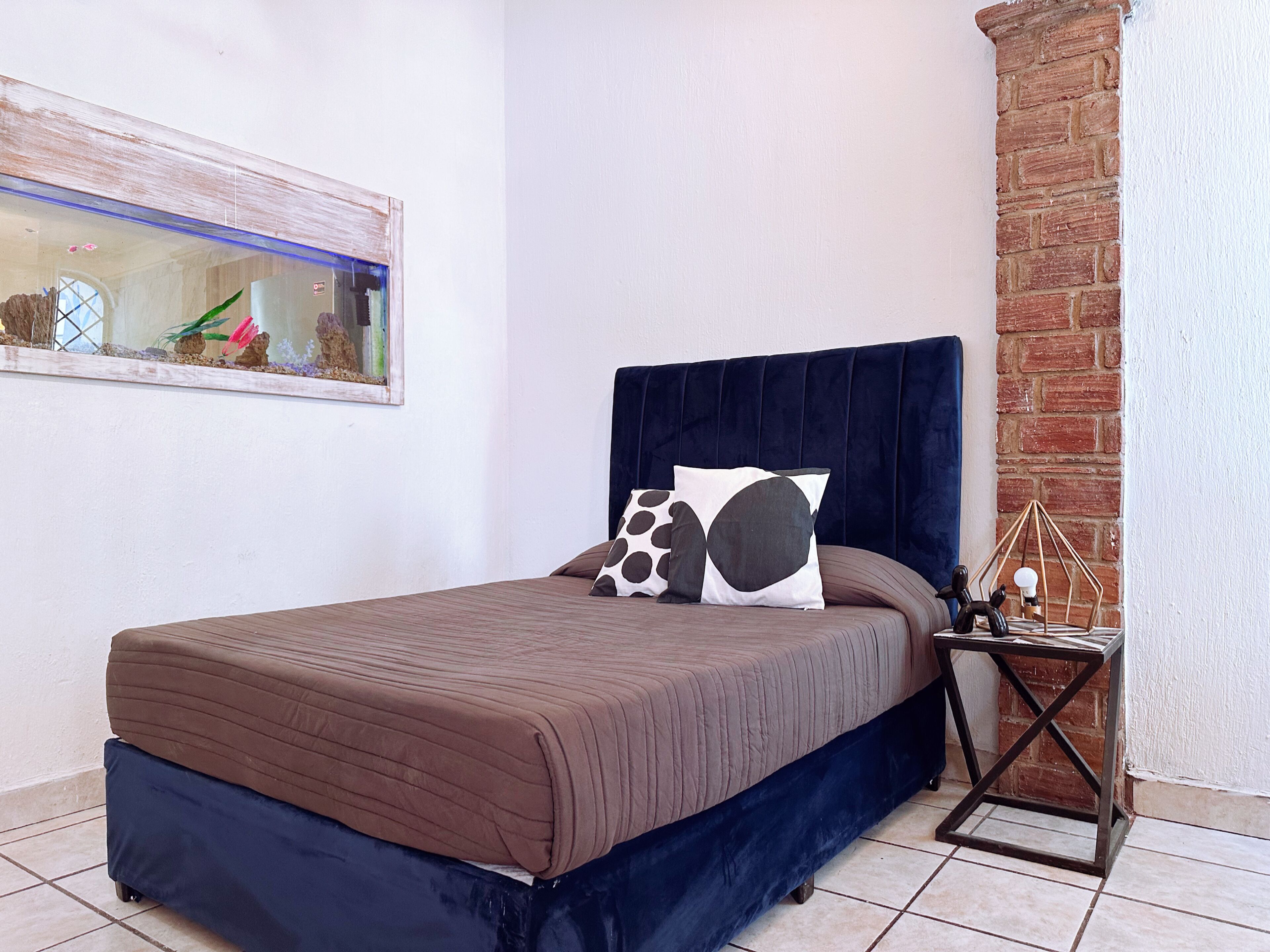 Een slaapkamer met een bed, nachtkastje, hangend kunstwerk en een bakstenen muur.