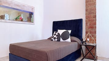 Een slaapkamer met een bed, nachtkastje, hangend kunstwerk en een bakstenen muur.