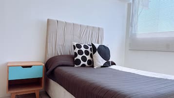 A bedroom with a bed, a nightstand, and a window with blinds.