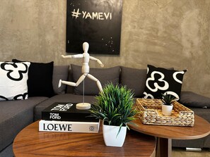 A wooden mannequin on a coffee table, a potted plant, a woven basket, and two books titled 'LOEWE' and 'TOM FORD' in a living room with a grey sofa and black and white patterned pillows. - Spacious 8-bedroom House in Central Guadalajara (Guadalajara)