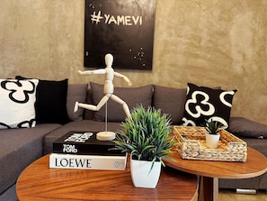 Una sala de estar con un maniquí de madera, una planta en maceta y libros sobre una mesa de centro.