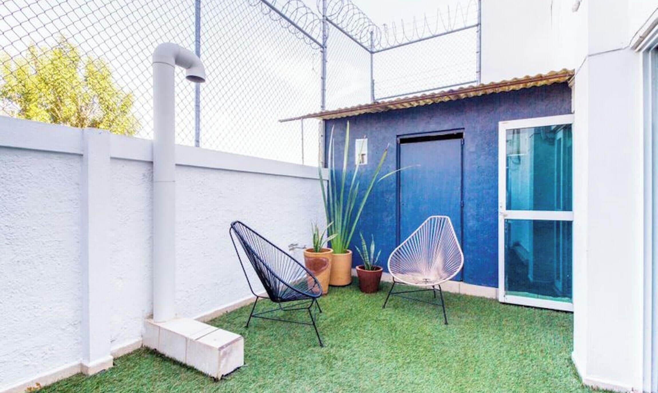 Een klein buitengebied met kunstgras, twee stoelen en potplanten.