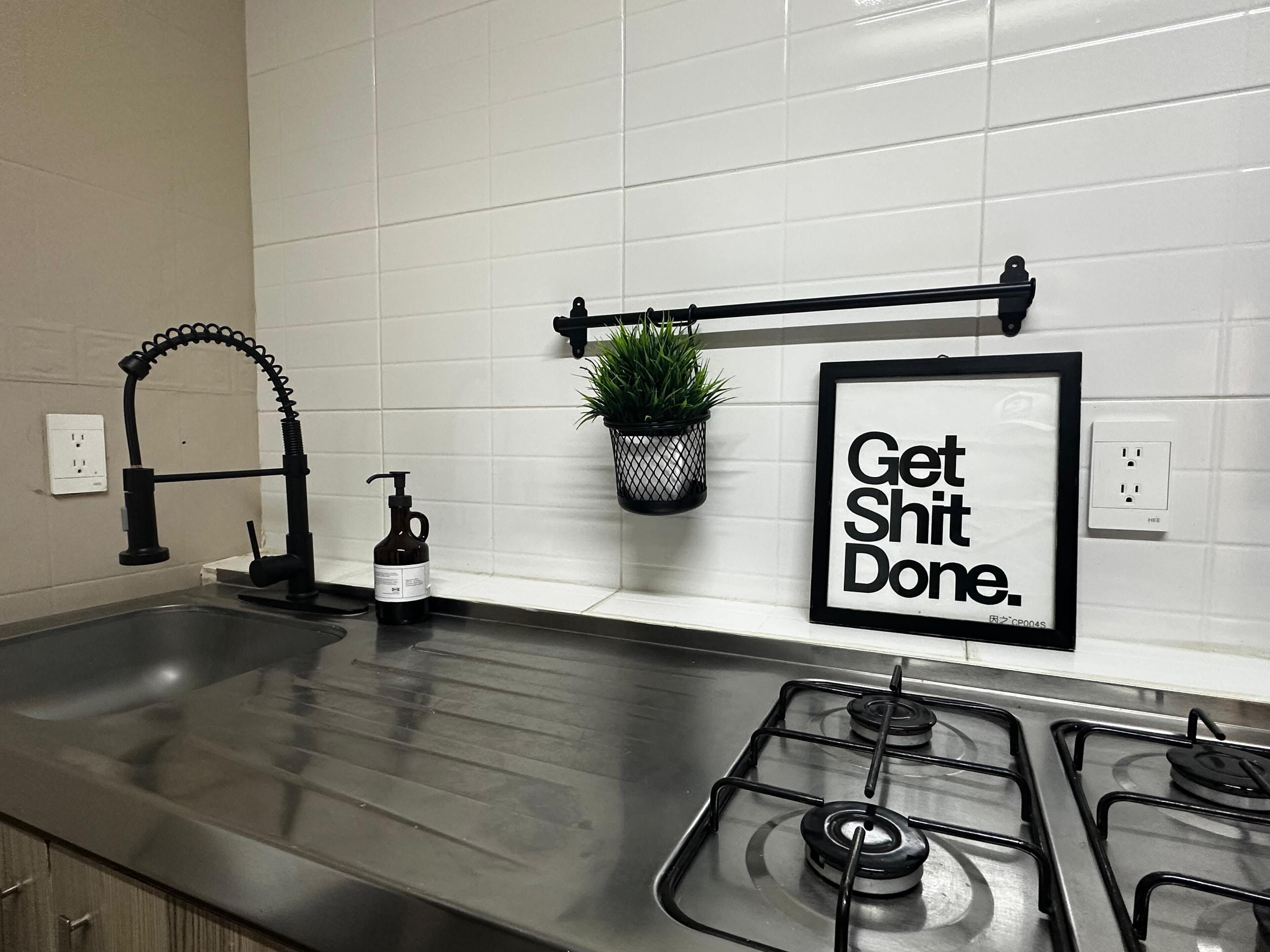Een keuken met een roestvrijstalen spoelbak, een kraan, een gasfornuis, een potplant en een inspirerend bord.