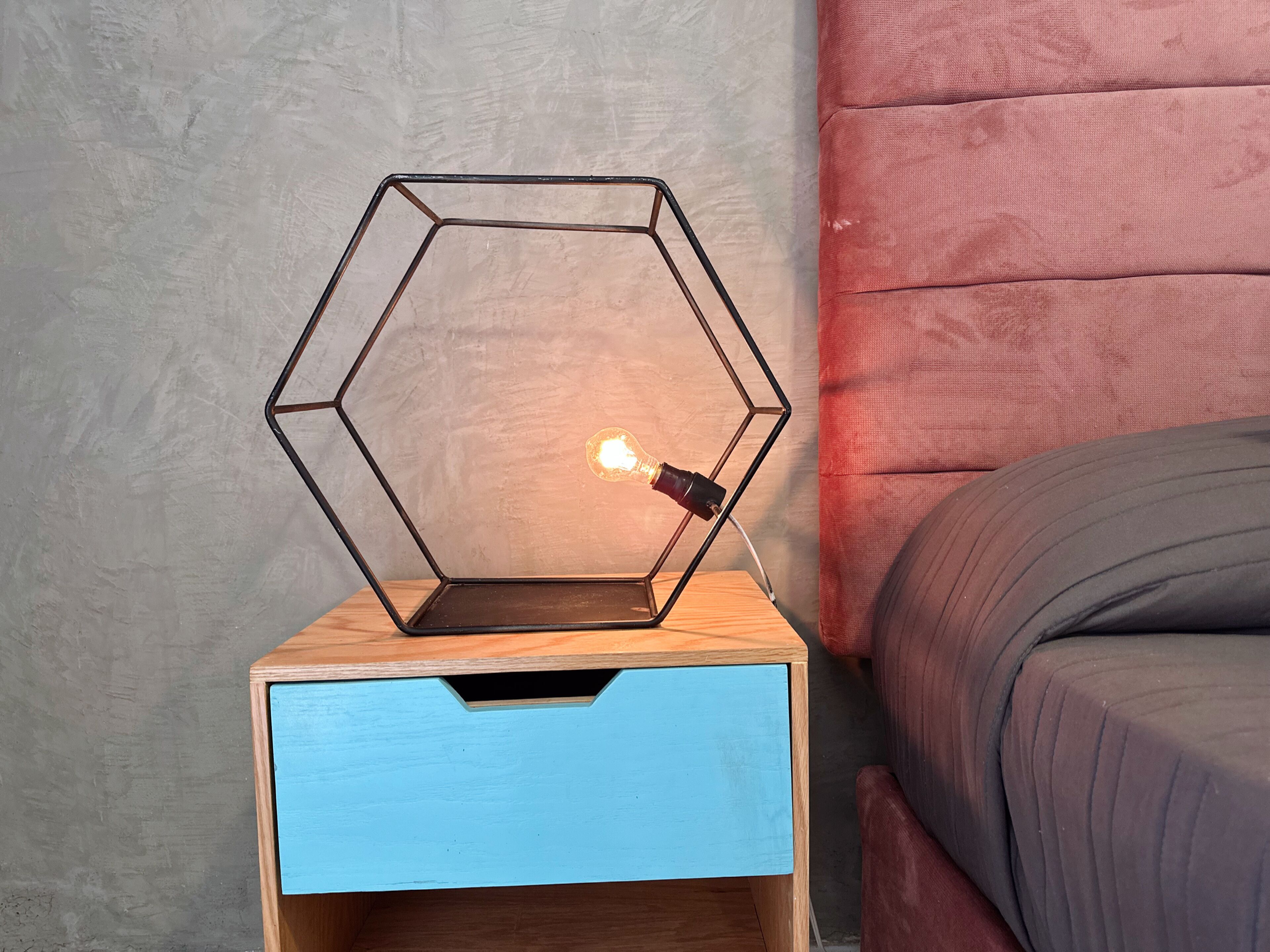 A hexagonal metal lamp on a wooden nightstand with a blue drawer.