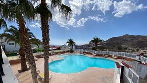 En swimmingpool omgiven av palmer, med utsikt över havet och ett bergigt landskap.