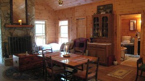 Interior acogedor de una cabaña con una mesa de comedor, sillas, chimenea y una pared de piedra.