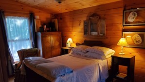 Un dormitorio rústico de madera con cama, dos lámparas de noche, una silla, un armario y una ventana con cortinas.