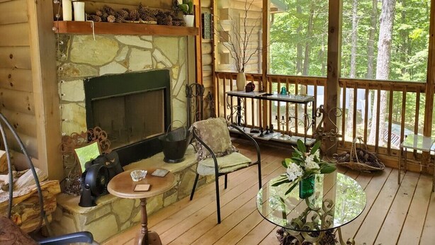 Interior acogedor de una cabaña con chimenea de piedra, terraza de madera y vistas al bosque.