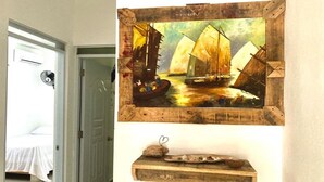 A bedroom with a bed, a door, and a wall-mounted painting of sailboats. - Family Suite - Apartment 1 in Villa Coconut (Samaná)