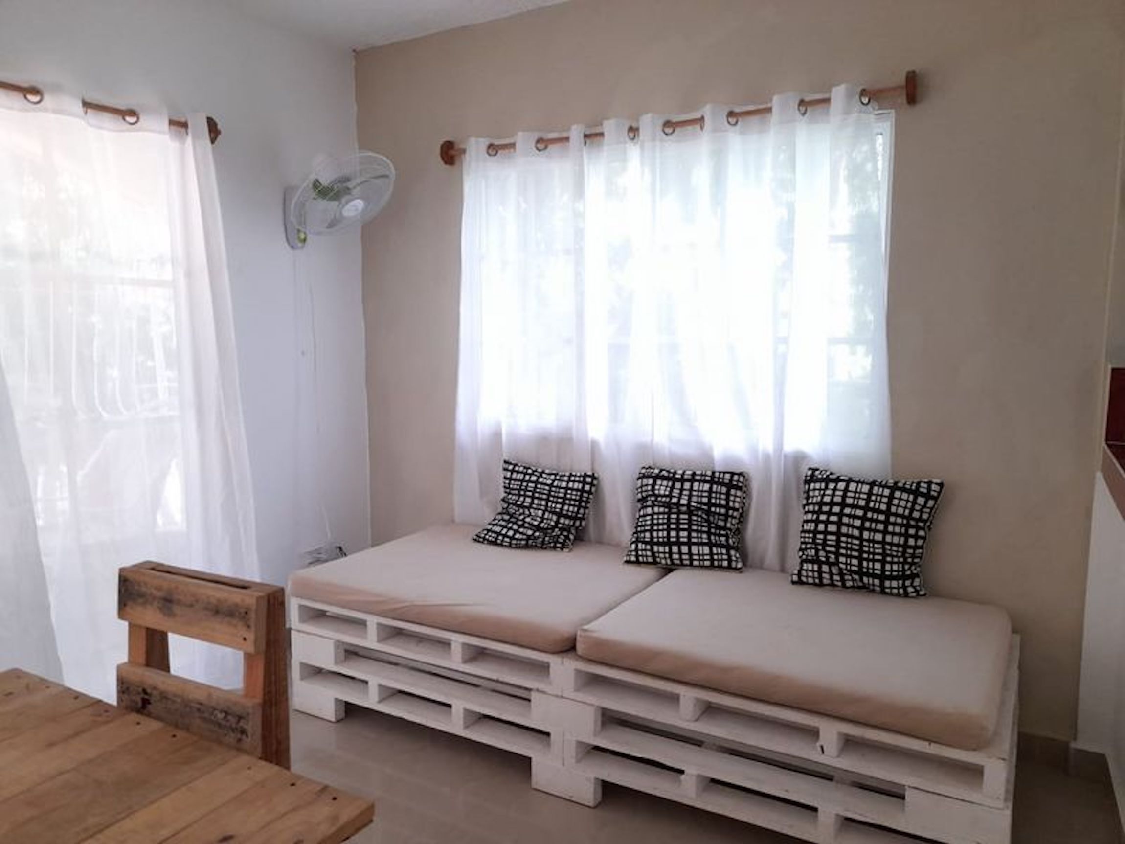 A room with a sofa bed, a wooden chair, and a fan.
