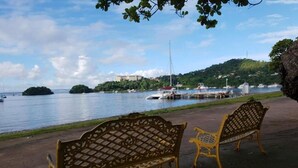 Two ornate benches facing a waterfront with boats and a hill in the background. - Family Suite - Apartment 1 in Villa Coconut (Samaná)