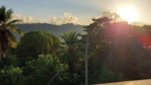 Ein hölzerner Balkon mit Blick auf eine tropische Landschaft und einen Sonnenuntergang.