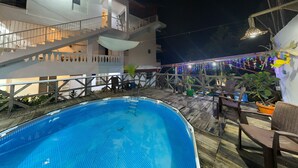 Ein Schwimmbad mit Holzterrasse, einer Treppe und einem Gebäude mit Balkonen.