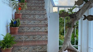 Eine Treppe mit gemusterten Fliesen führt zu einer roten Tür, umgeben von Topfpflanzen und einem Ast mit fischförmigen Verzierungen.