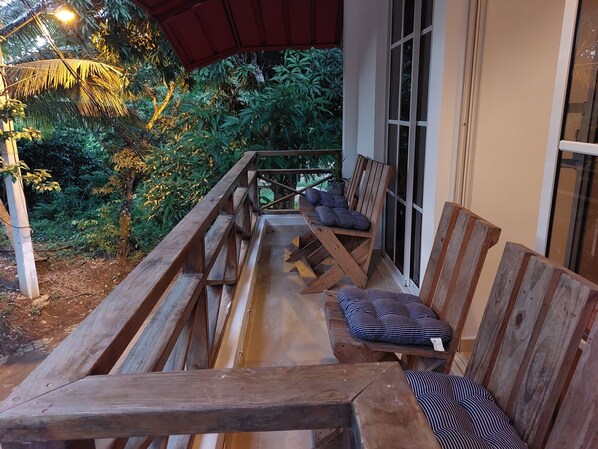 A wooden deck with benches and a table, surrounded by lush greenery and a red awning. - Family Apartment - Apartment 5 in Villa Coconut (Samaná)