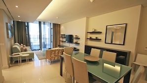Moderni olohuone, jossa on lasinen ruokapöytä, beigenväriset tuolit, sohva ja televisio.