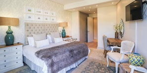 Quarto com cama grande, mesas de cabeceira, escrivaninha e uma cadeira.